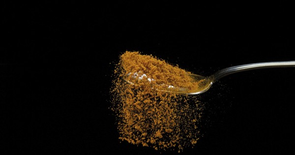 Spoon and Curry Powder falling from Spoon against Black Background