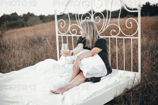 Full body barefoot female with blond hair enjoying wine and looking away while sitting on