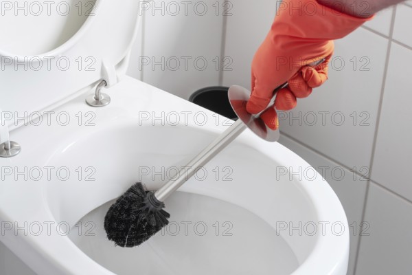 person wearing rubber gloves cleaning toilet bowl with toilet brush
