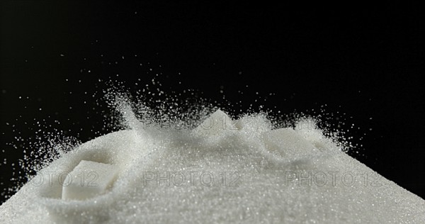 White Sugar Cube falling on Powder Sugar against Black Background