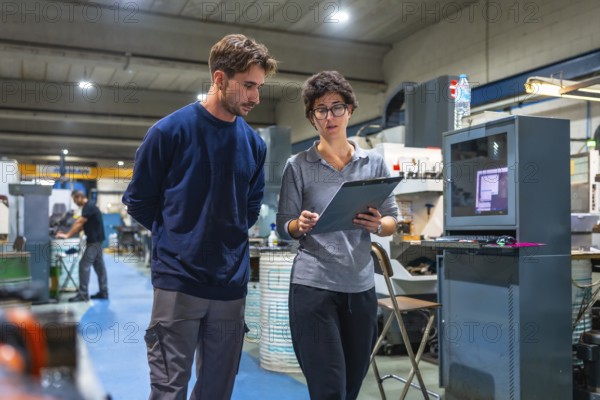 Female manager and male young engineer doing paperwork standing and talking at factory