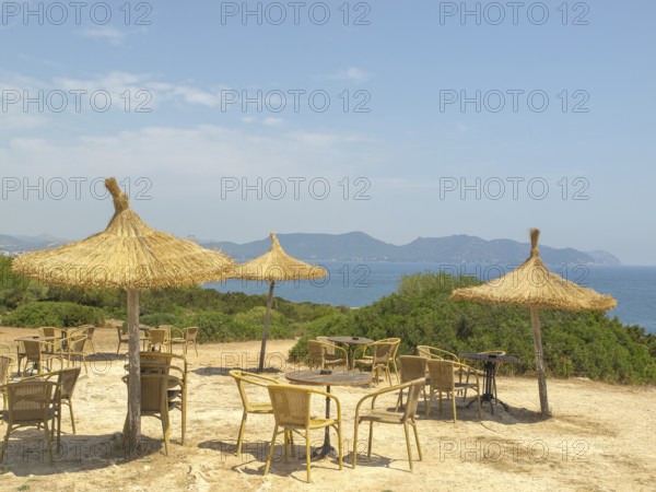 Beach huts with straw parasols, tables and chairs, sea view and mountains in the background in