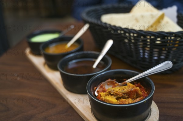 Indian dip, relish, chutney and sauce served in small black bowls with crispy papadam bread on a