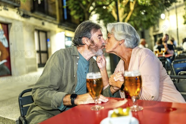 Senior cute couple kissing while drinking beer in an outdoor terrace in the city street