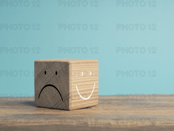 A wooden cube with light and dark side, once with smiling face and with sad face, There is always