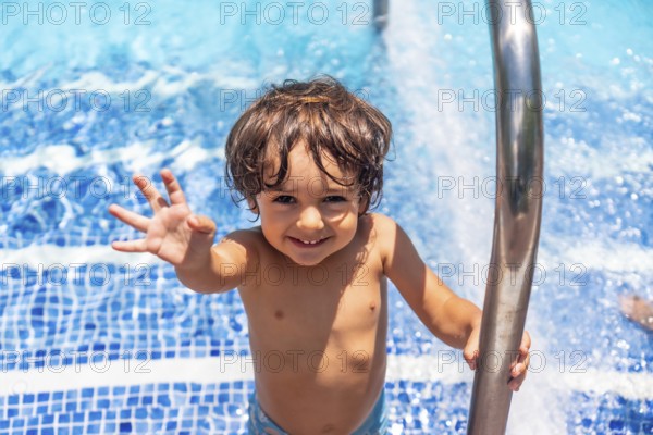 Two year old boy enjoying summer in a swimming pool, smiling on vacation from the water