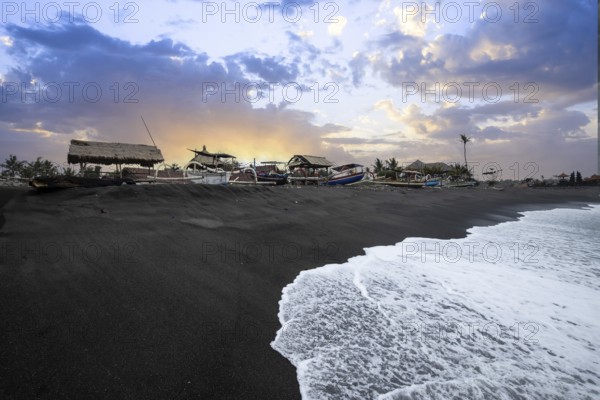 Traditional fishing boat Jukung, on a black sand beach directly by the sea. Sunset landscape by the