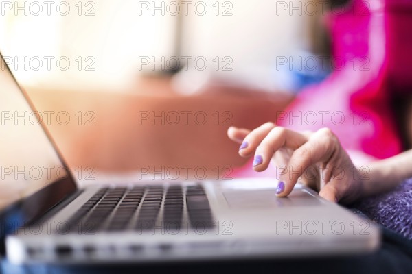 Girl with purple fingernails is using her laptop at home on the couch