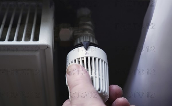 hand turning off thermostat on radiator to save energy due to increasing heating costs