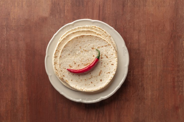 A red chili pepper, shot from above on a pile of tortillas, Mexican flatbreads, on a dark rustic
