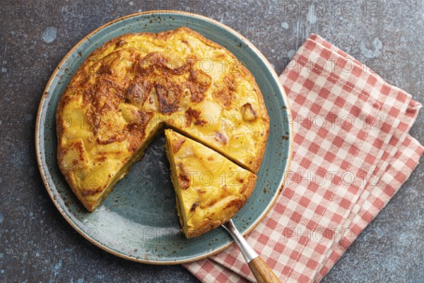 Homemade Spanish tortilla with one slice cut - omelette with potatoes on plate on stone rustic