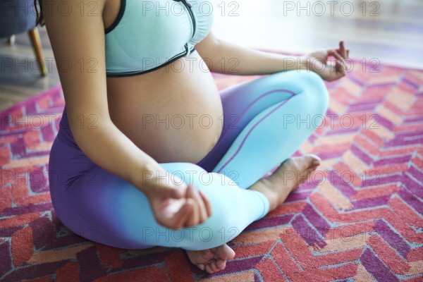 Close-up of pregnant sporty woman practicing yoga, meditating in Lotus pose Padmasana. Conscious
