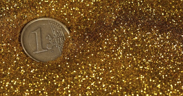 Coin of 1 Euro Rolling on Gold Powder against Black Background