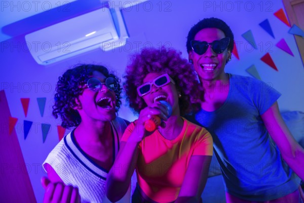 Happy multi-ethnic friends singing karaoke at night partying together at the apartment