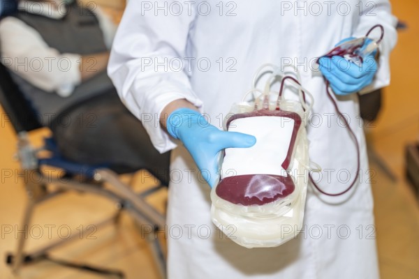 Part of and close-up of a healthcare worker showing a blood bag filled with a donation
