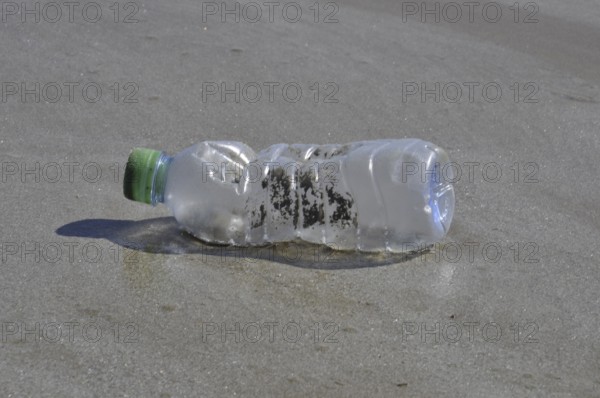 A plastic bottle with a green cap lying on wet sand, representing pollution on a beach