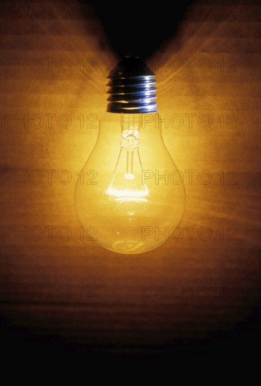 Closeup of an old burning light bulb, switched on, a carton as background is illuminated, lit with