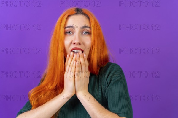 Redhead woman in studio photography making the gesture please on a purple background