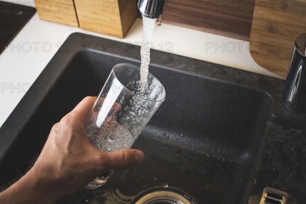 Filling glass of water from stainless steel kitchen faucet. Drinking water concept. Austria pure