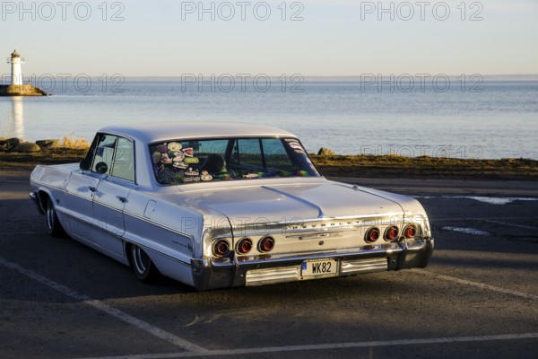 American classic car, Chevrolet Impala from 1964, behind the lake Vättern and the lighthouse of