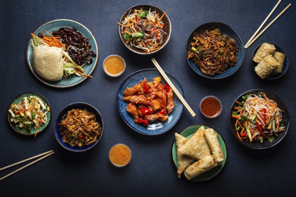Set of assorted Chinese dishes on table: sweet and sour chicken on plate, fried spring rolls,