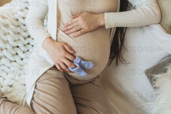 Maternity and pregnancy concept. Cropped photo of pregnant woman holding pair of cute blue baby
