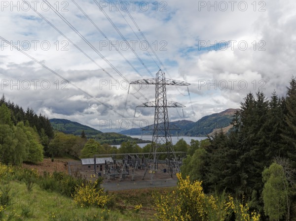 A power station in the middle of a natural landscape with electricity pylon and cloudy sky,