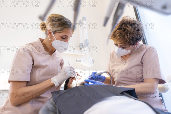 Dentist and assistant performing a mouth and tooth filling on a young client in the modern dental