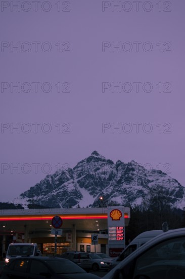 Shell petrol station in the foreground at dusk, snow-covered Serles mountain peaks in the