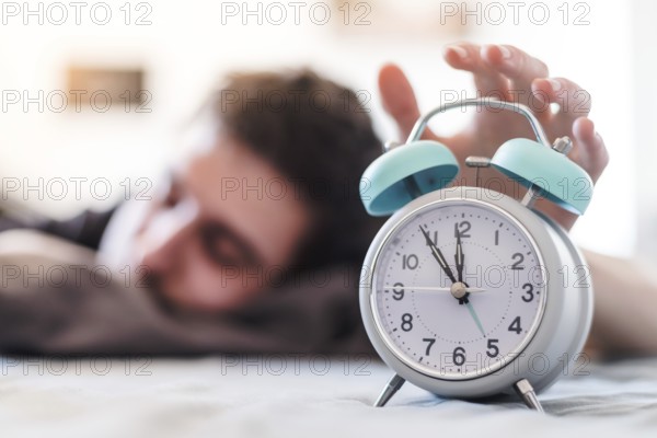White alarm clock in the morning. Young man wakes up