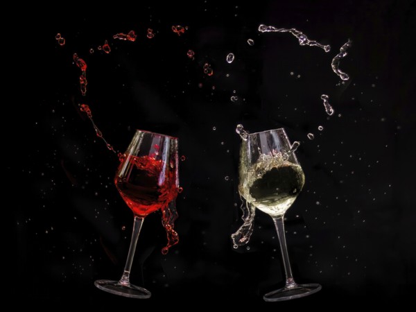 Two clinking wine glasses with red and white wine splashing out, captured in dynamic movement