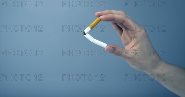 Hand breaking a cigarette against blue background