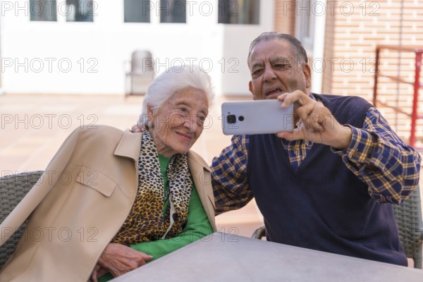 Two very happy elderly people in the garden of a nursing home, looking at the phone