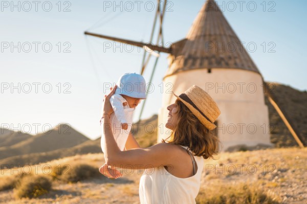 Mother raising a baby in arms next to a windmill in Cabo de Gata, Spain, Europe