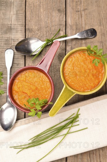 Top view of two rustic bowls with carrot soup on a wooden table