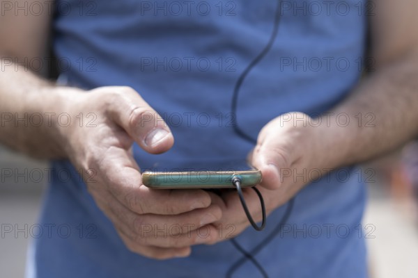 Close-up of a man's hands holding his phone with the headphones connected