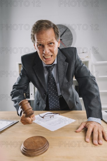 Angry mature judge striking his gavel table courtroom