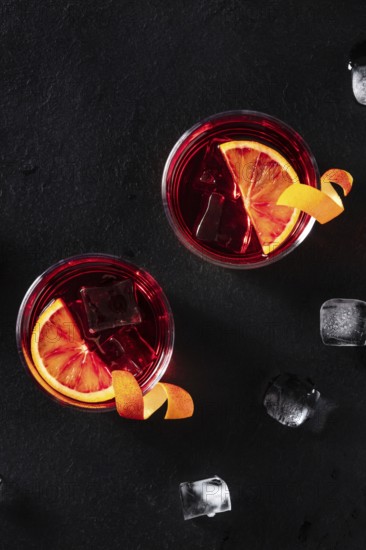 Negroni cocktails with orange rind, shot from the top with ice cubes on a black background, with
