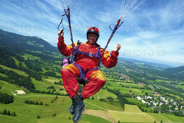 A paraglider in orange and red overall flies over the meadows at Brauneck near Lenggries, Bavaria,