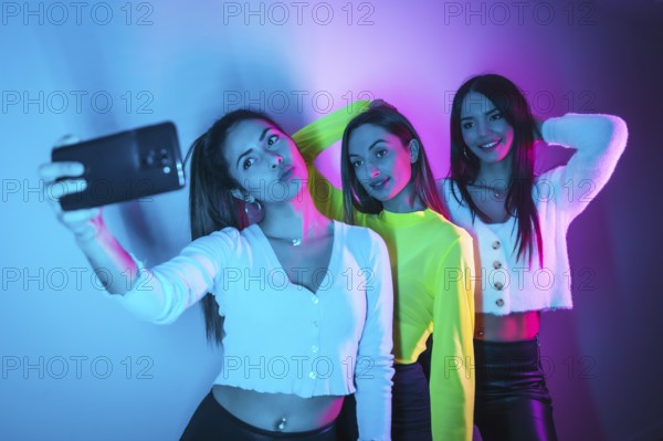 Lifestyle of friends partying in a nightclub with blue and pink neon lights, taking a selfie with