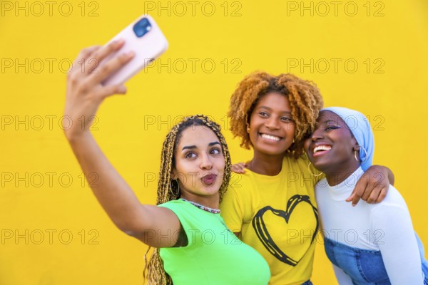 Portrait with copy space of three female friends taking a selfie together in a yellow background