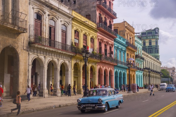 A blue oldtimer taxi is driving through Habana Vieja in front of a colorful facade of colonial
