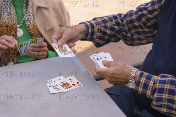 Hands of two elderly people in the garden of a nursing home or retirement home playing cards on a