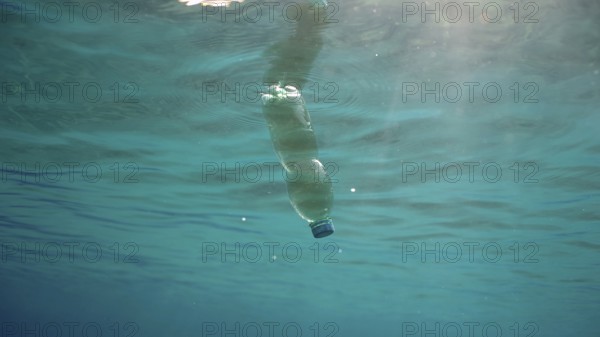 Green plastic bottle drifting under surface of blue water. Plastic pollution of Ocean, Discarded