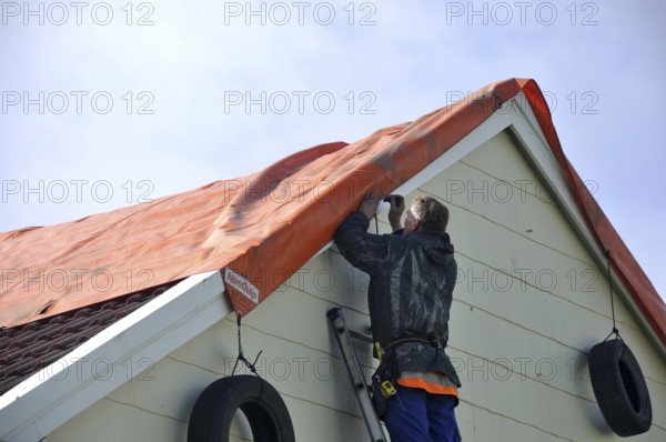 GREYMOUTH, NEW ZEALAND, APRIL 17, 2014: Volunteer worker places a tarpaulin on a house de-roofed in