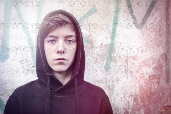 Portrait of a teenage boy with black hoodie in front of a graffiti