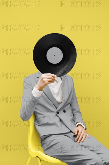 Man covering his face with vinyl record while wearing ultimate gray clothes. High resolution photo