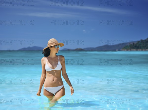 Sexy young woman in straw hat and white bikini on tropical paradise beach. Summer vacation, travel