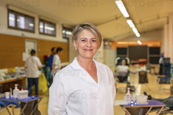 Portrait of a happy female blonde adult doctor in white lab coat in a blood donation center
