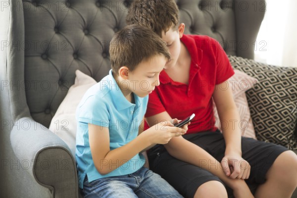 Older brother on the sofa and younger brother playing mobile phone. Family portrait